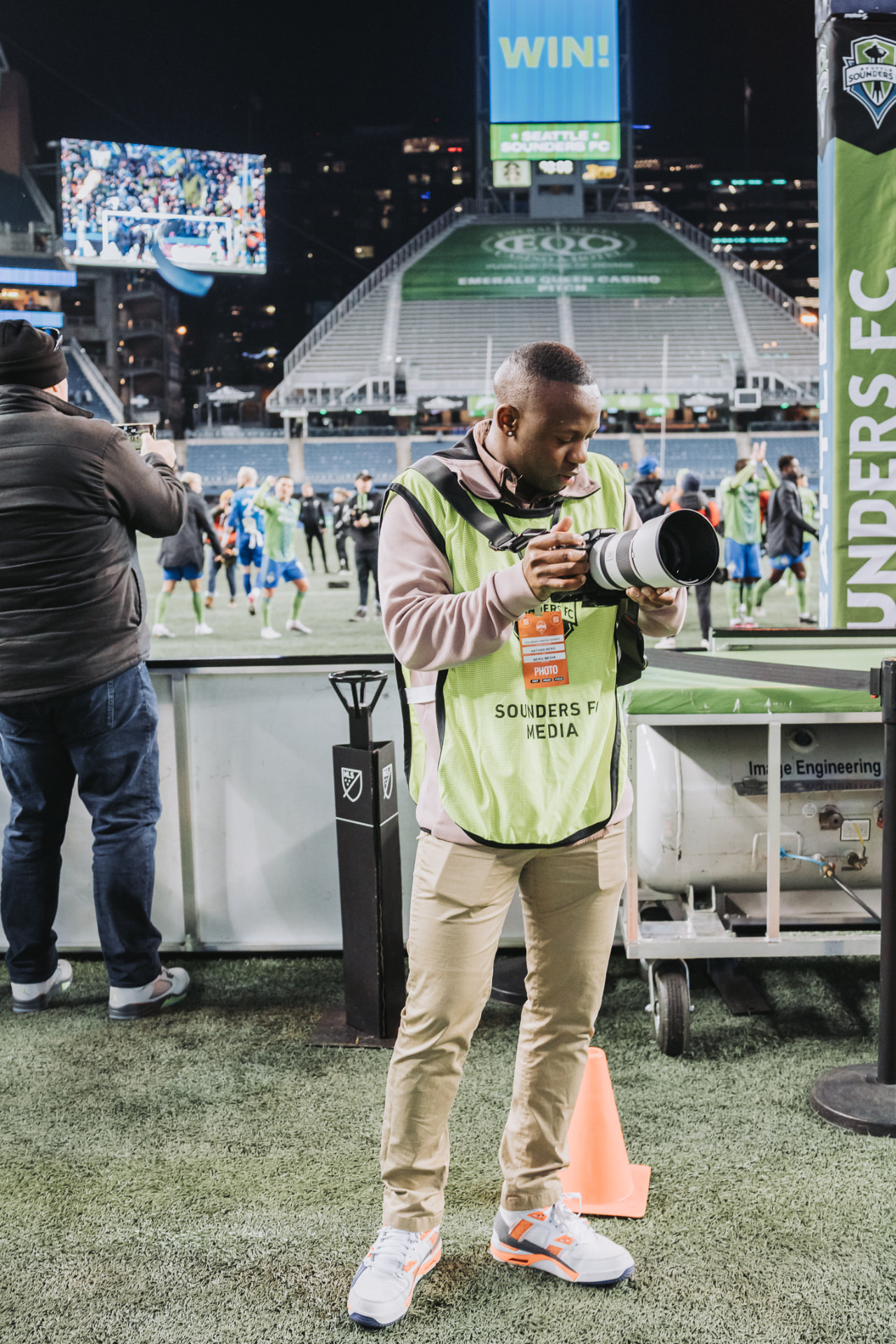 Nathan Berg checking his camera on the pitch at a Seattle Sounders match, wearing a Sounders FC media vest.