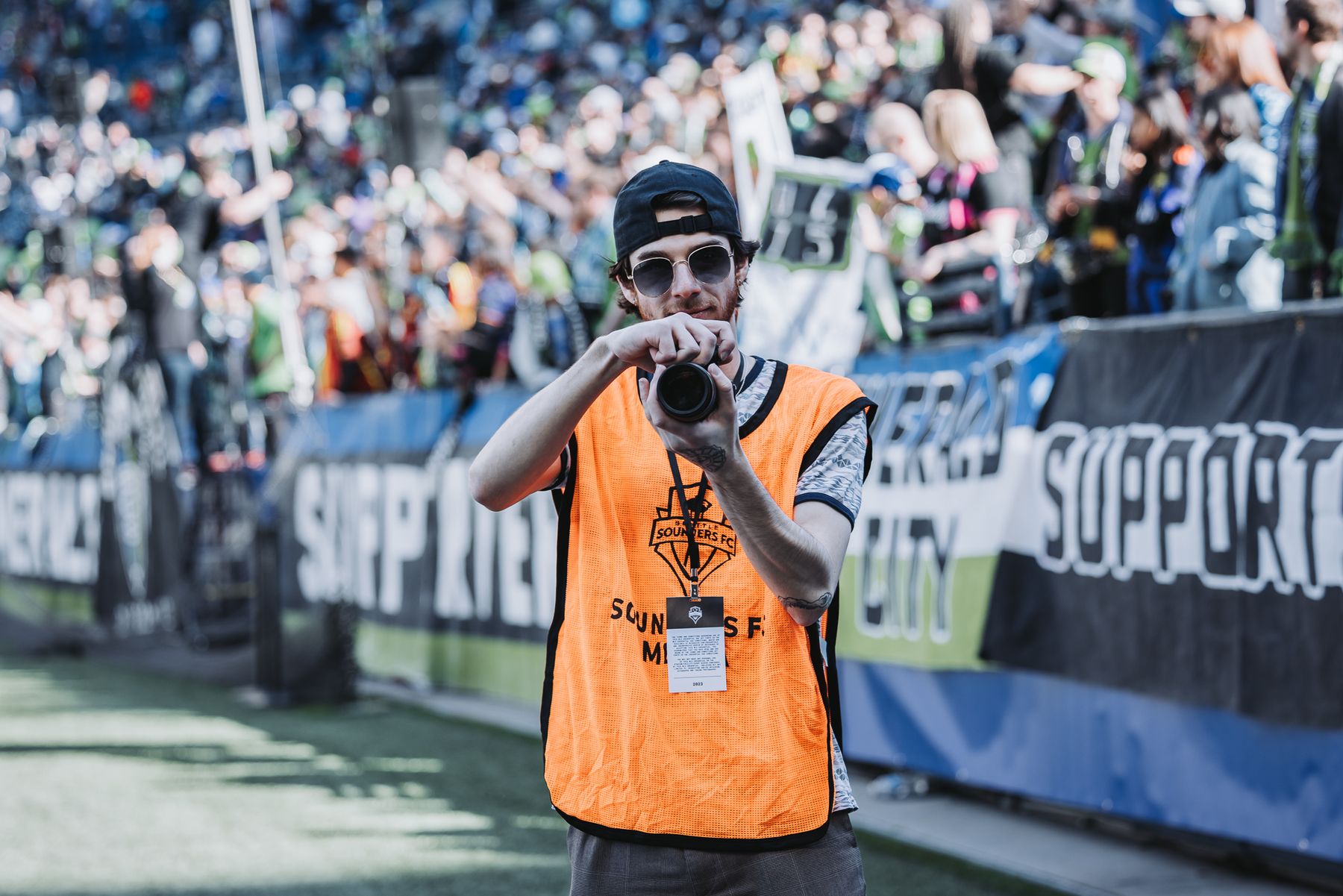 Alec Hoffman raises his camera toward the lens in front of the supporters' section banners at Lumen Field.