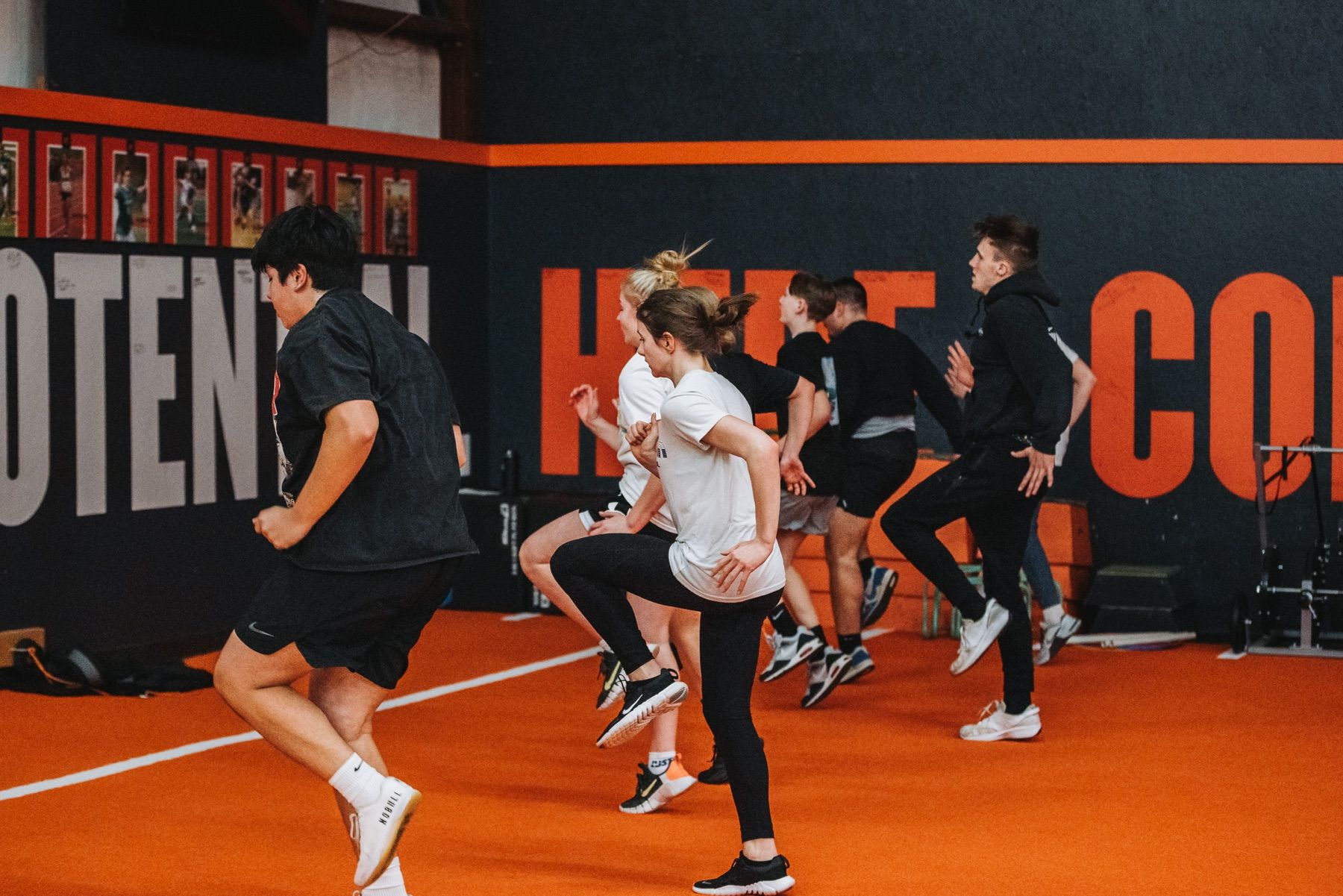 Athletes move through a high-knee warm-up on an orange indoor training floor.