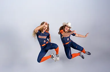 Two athletes in navy and orange leap mid air on a white studio backdrop