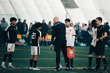 Youth soccer players and a referee line up on turf inside a sports dome