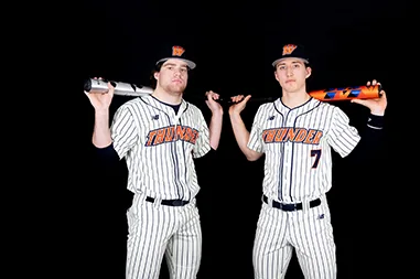 Two baseball players in pinstripes pose with their bats on a black backdrop