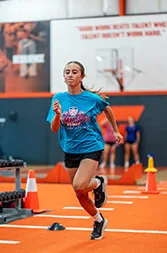 A young athlete in a blue shirt sprints across an orange training floor