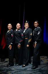 Navy sailors in dress uniforms stand in a row