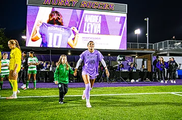 A women's soccer player runs out as her name lights up the video board