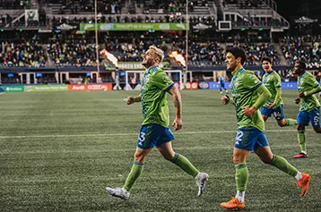 Seattle Sounders players walk across the pitch as flames fire behind them