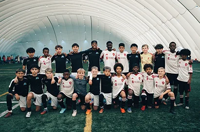 A youth soccer team poses together on turf inside a sports dome