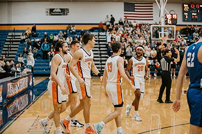 College basketball players in white and orange during a game in a packed gym