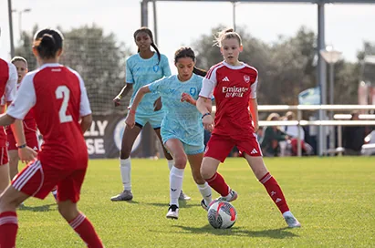 Youth soccer players in red and light blue chase the ball