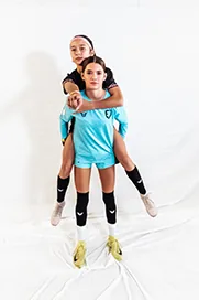 Two young players in light blue pose together on a white backdrop