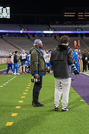 People walk across a football field inside a stadium