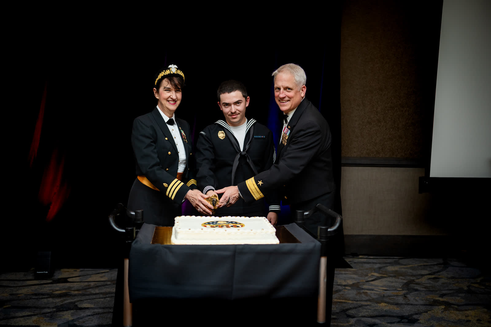 Two officers and a sailor cut the ceremonial cake together at the Navy Ball in Everett.