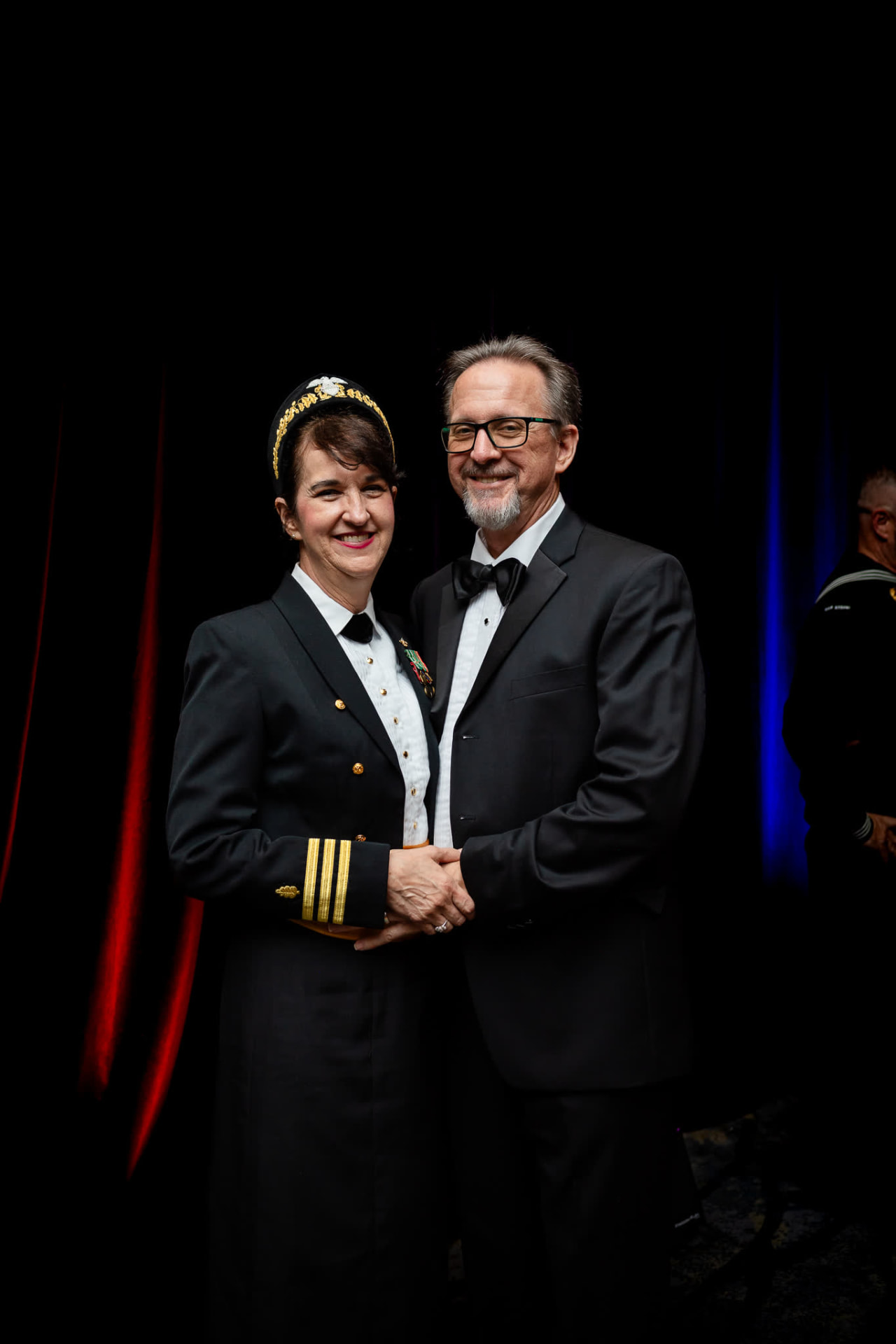 An officer in dress uniform and her partner in black tie pose together at the Navy Ball.