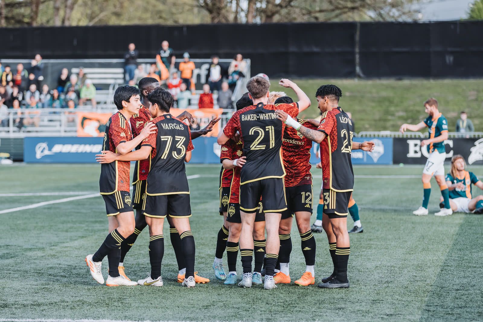 Sounders players gather in a tight huddle on the pitch after a goal.
