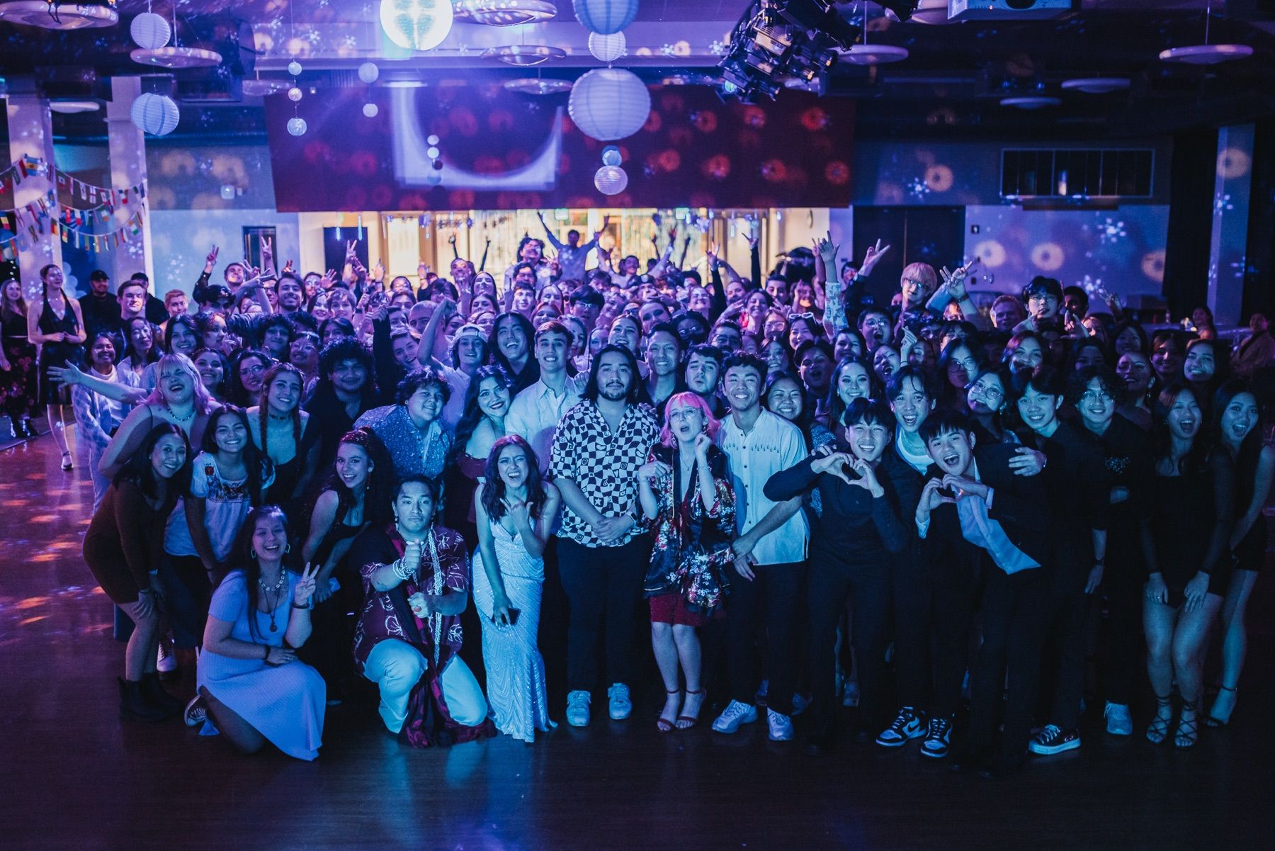 Large group poses beneath blue and purple lights at a winter-themed dance.