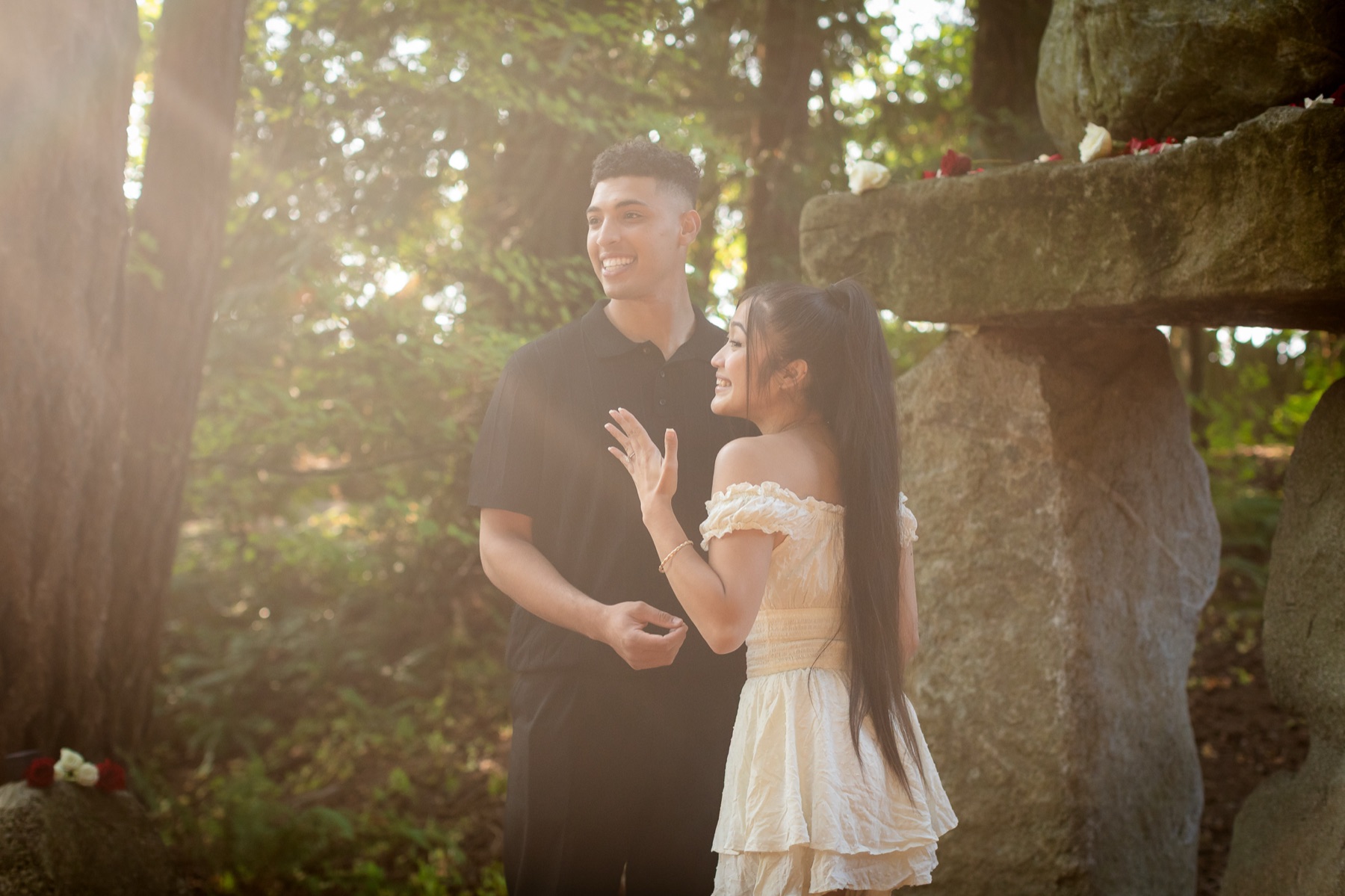 Trevor and Jocelyn laugh together in low sun, her hand raised to show the ring.