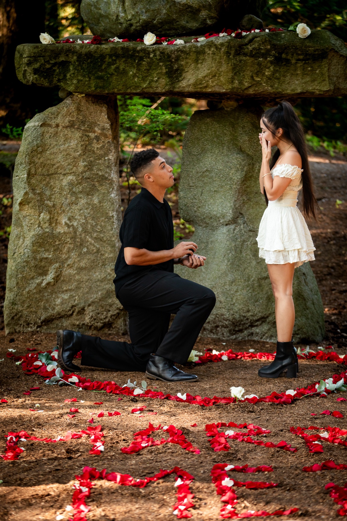 Trevor kneels with the ring inside a heart of rose petals as Jocelyn covers her face.